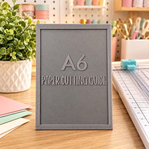 May include: A rectangular gray A6 paper cutting guide with a textured surface. The text A6 and PAPER CUTTING GUIDE are embossed in the center of the tool. The guide features a thin raised border around the entire perimeter of the object.