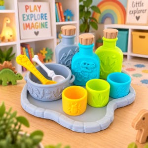 May include: A dinosaur-themed silicone feeding set featuring a light blue tray, a bowl with embossed tracks, two spoons, three small cups in yellow, green, and blue, and two bottles with cork-style lids featuring dinosaur and mountain motifs.