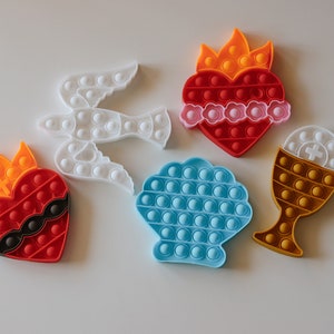May include: Five colorful silicone pop-it toys shaped like a dove, a heart with flames, a seashell, a heart with thorns, and a chalice.
