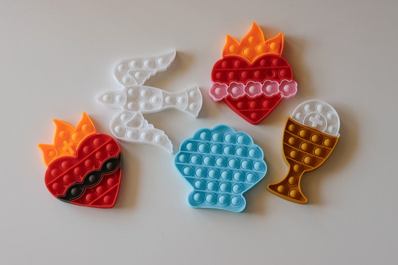 May include: Five colorful silicone pop-it toys shaped like a dove, a heart with flames, a seashell, a heart with thorns, and a chalice.