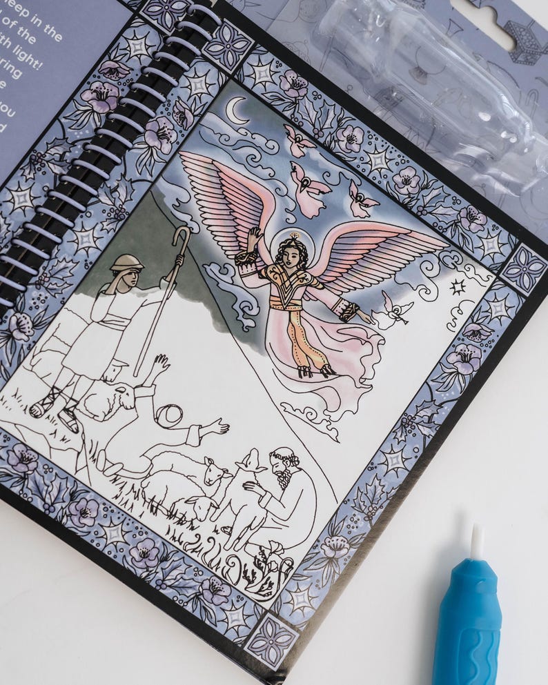 May include: A spiral-bound art kit featuring a religious illustration of an angel with pink wings, surrounded by other figures and sheep. The artwork is framed with a floral and geometric border. A blue tool is visible.
