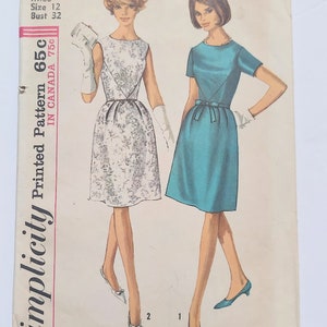 May include: A Simplicity sewing pattern envelope 6220 for a dress in size 12 with a 32-inch bust. The illustration shows two variations of a knee-length dress: one with a floral print and one in solid teal, both featuring a fitted waist and bow detail.