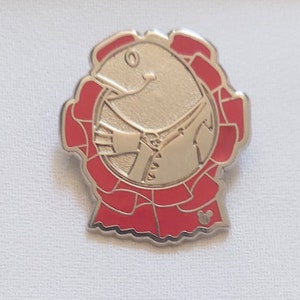 May include: A silver-colored pin featuring a smiling cartoon character in a red outfit. The character is surrounded by a red, scalloped border. A small Mickey Mouse icon is visible at the bottom.
