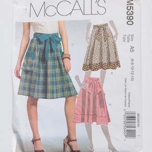 May include: McCall's sewing pattern M5390 featuring three skirt designs. One skirt is plaid, another has a floral pattern, and the third has red and white stripes. The pattern size is A5, and the measurements are (6-8-10-12-14).