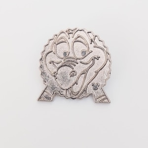 May include: A silver-colored pin featuring a cartoon character with a smiling face, large eyes, and a textured border. The pin has a Disney logo on the bottom right and is set against a white background.