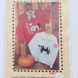 May include: A sewing pattern packet titled Barnyard Bessie by Bear Thread Designs. The cover features a red sweatshirt with a barn graphic and a white sweatshirt with a cow graphic, both with collars and pockets. A pumpkin sits at the bottom.