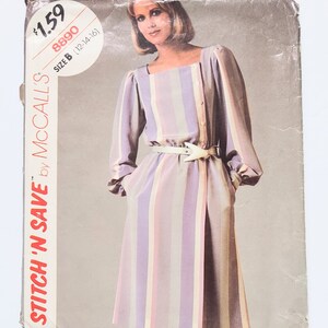 Könnte beinhalten: Vintage McCall's Schnittmuster für ein Kleid mit vertikalen Streifen in Lavendel, Rosa und Beige. Das Muster hat einen quadratischen Ausschnitt, lange Ärmel und einen weißen Gürtel. Die Verpackung ist mit "Stitch 'N Save" und Größe B (12-14-16) gekennzeichnet.