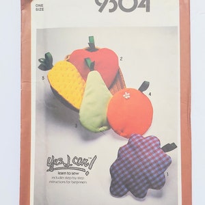 May include: Simplicity 9304 sewing pattern featuring fabric fruit shapes. The pattern includes a red apple, green pear, orange, yellow pineapple, and a purple and blue checkered grape. The text "Yes I can!" is also visible.