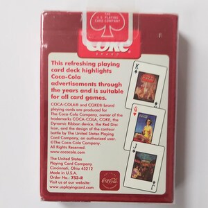 K&ouml;nnte beinhalten: Ein versiegeltes Kartenspiel von Coca-Cola in einer roten Schachtel. Die Schachtel zeigt das Coca-Cola-Logo und Text, der Vintage-Werbung hervorhebt. Die Karten zeigen klassische Coca-Cola-Bilder. Hergestellt von The United States Playing Card Company.