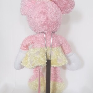 May include: A pink plush toy mouse with a yellow bow and polka-dot skirt. The toy has white gloves and is mounted on a brown stand. The toy is approximately 10 inches tall.