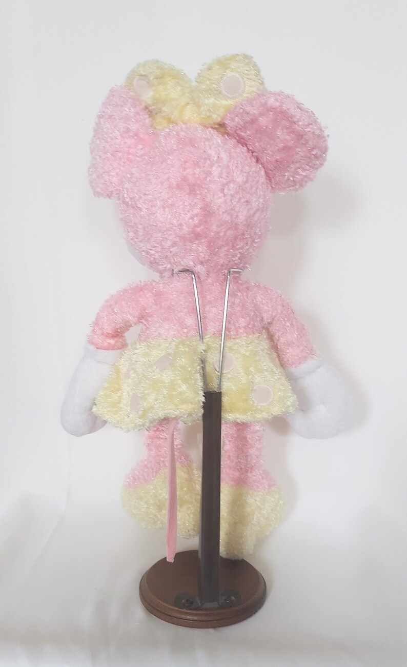 May include: A pink plush toy mouse with a yellow bow and polka-dot skirt. The toy has white gloves and is mounted on a brown stand. The toy is approximately 10 inches tall.