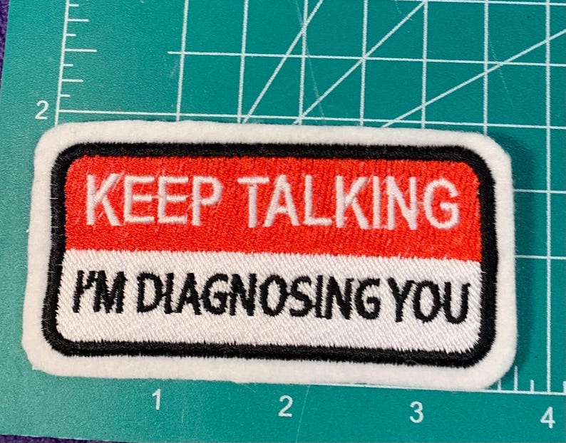 Puede incluir: Parche blanco bordado con borde negro. El parche tiene texto rojo y blanco que dice "KEEP TALKING I'M DIAGNOSING YOU".