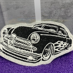 May include: Black and white embroidered patch of a vintage car with flames coming out of the back tire. The car is outlined in white and the background is gray.