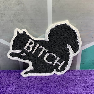 May include: Black embroidered patch shaped like a squirrel with the word "BITCH" in white lettering.