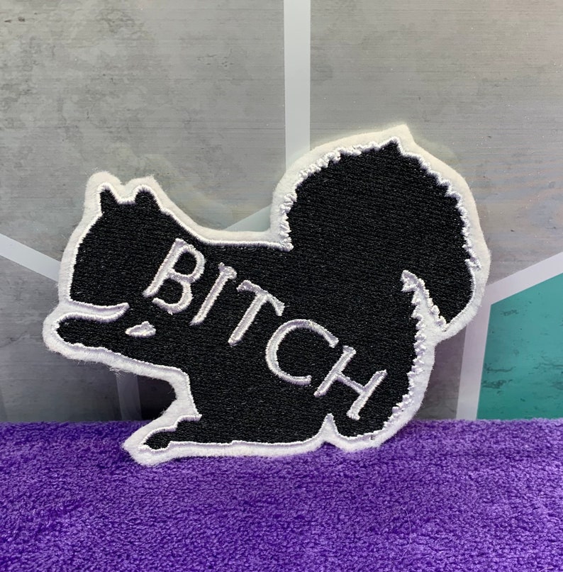 May include: Black embroidered patch shaped like a squirrel with the word "BITCH" in white lettering.
