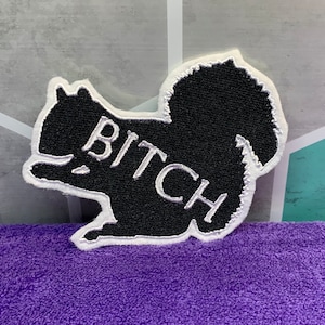 May include: Black embroidered patch shaped like a squirrel with the word "BITCH" written in white on the side.
