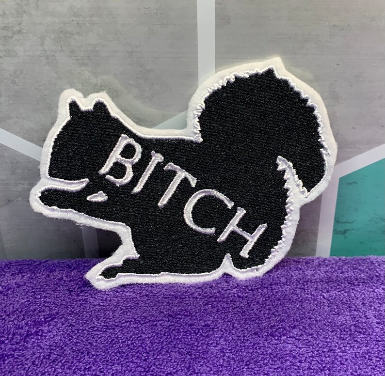 May include: Black embroidered patch shaped like a squirrel with the word "BITCH" written in white on the side.