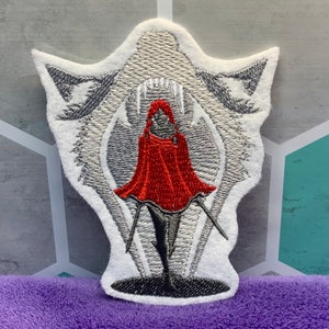 May include: Embroidered patch featuring a white wolf head with an open mouth, a red hooded figure standing inside the wolf's mouth, and a white background.