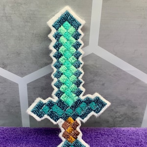 May include: A green and blue embroidered Minecraft sword patch with a white outline.