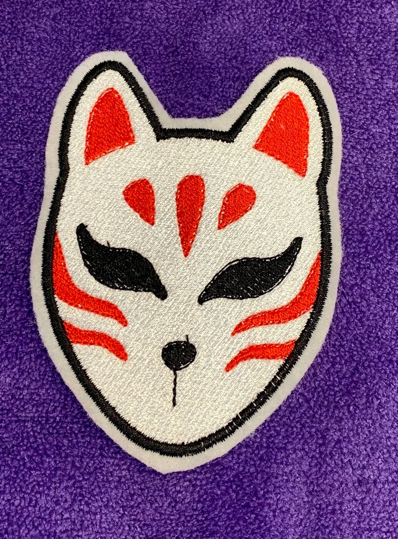 May include: White embroidered fox mask with red and black details. The mask is on a purple background.