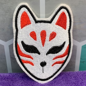 May include: White embroidered patch with a red and black fox mask design. The mask has a stylized fox face with red ears, eyes, and markings.