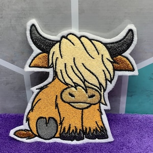 May include: A brown and white embroidered patch of a cartoon Highland cow with a fluffy mane. The cow is sitting with its legs tucked under its body.