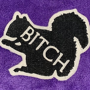 May include: Black embroidered patch of a squirrel with the word "BITCH" written in white on its body.
