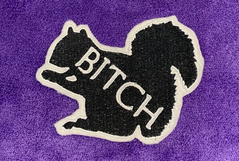 May include: Black embroidered patch of a squirrel with the word "BITCH" written in white on its body.