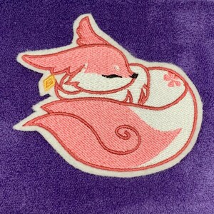 May include: Embroidered patch of a sleeping pink fox with white accents, a gold detail, and a flower. The fox is set against a purple background. The patch is outlined in white.