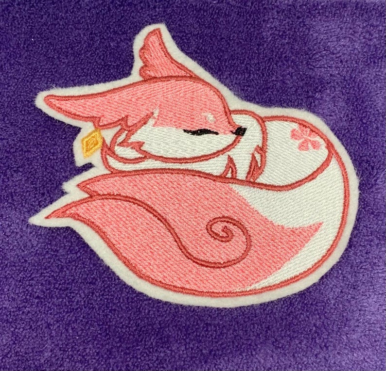 May include: Embroidered patch of a sleeping pink fox with white accents, a gold detail, and a flower. The fox is set against a purple background. The patch is outlined in white.