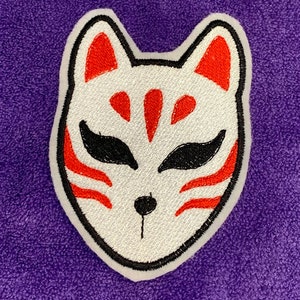 May include: White embroidered fox mask with red and black details. The mask is a traditional Japanese kitsune mask.