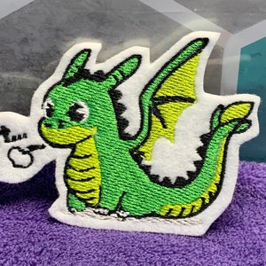 May include: Green embroidered iron-on patch of a cartoon dragon with a yellow wing and the text "PFFF..." in a speech bubble.