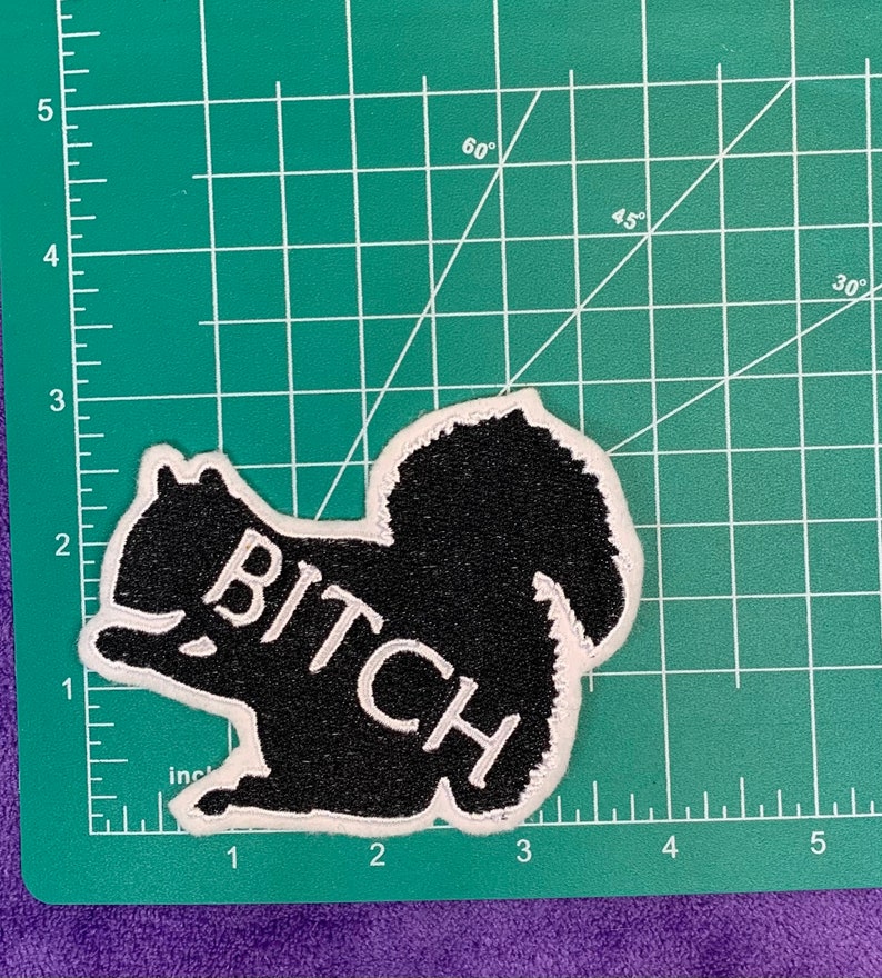 May include: Black and white embroidered patch of a squirrel with the word "BITCH" written across its body.