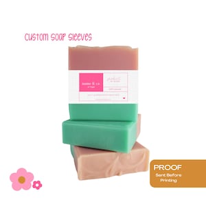 May include: Stacked bars of soap in shades of pink and green, with a white label wrapped around the top bar. The label has text that reads "name & co. or logo" and "100% natural". The words "custom soap sleeves" are in pink text at the top.