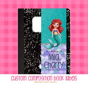 May include: A composition notebook with a custom label featuring a cartoon mermaid with red hair and a teal tail. The label reads "This belongs to Mila Charry Kindergarten." The notebook has a black and white speckled cover and the text "CUSTOM COMPOSITION BOOK LABELS".