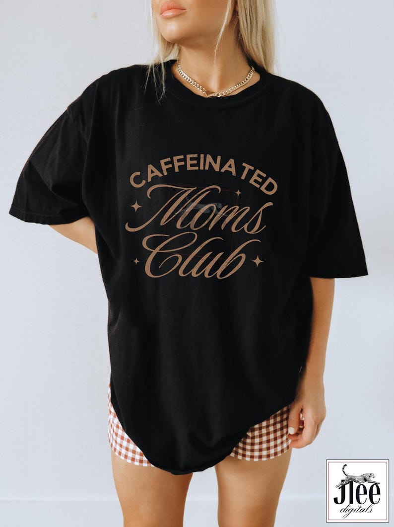 Op de afbeelding: Zwart oversized T-shirt met de tekst "caffeinated moms club" in bruine cursieve letters met sterren aan beide kanten van de tekst.