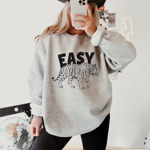 May include: A gray sweatshirt with a black and white tiger graphic and the word "EASY" printed on the front.