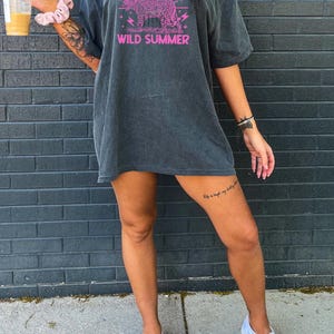 May include: A dark gray oversized t-shirt with a pink graphic of a leopard with the text "WILD SUMMER" printed on the front.