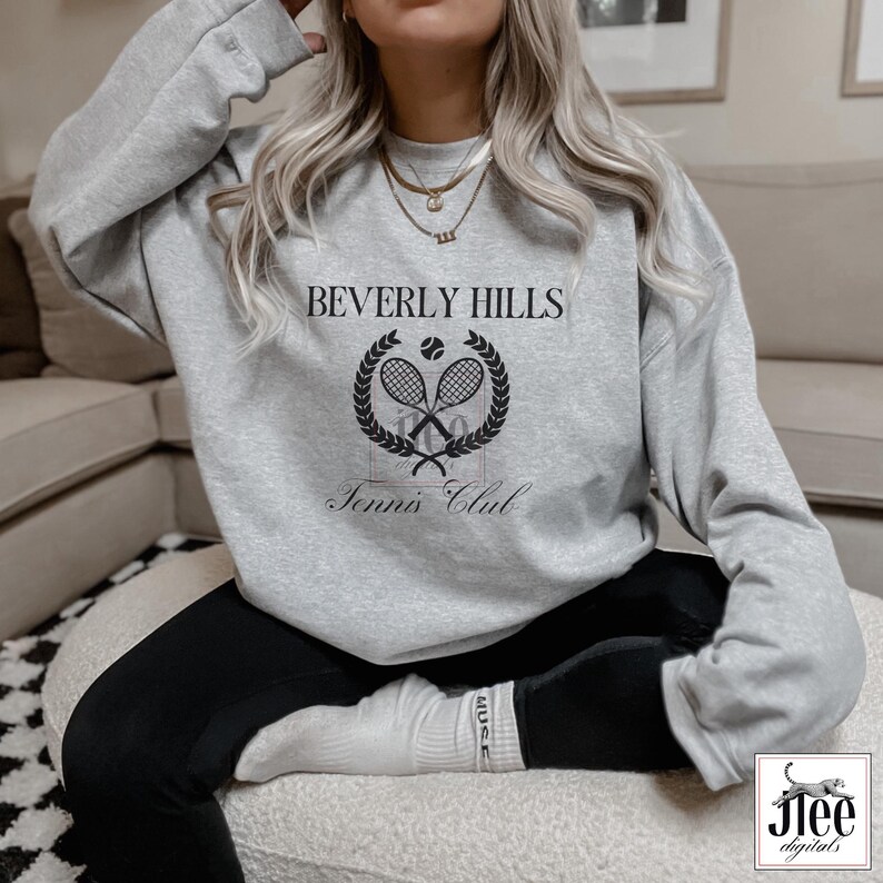 Puede incluir: Una sudadera gris con el texto "Beverly Hills Tennis Club" impreso en la parte delantera. El dise&ntilde;o presenta una raqueta de tenis y una pelota dentro de una corona de laurel.