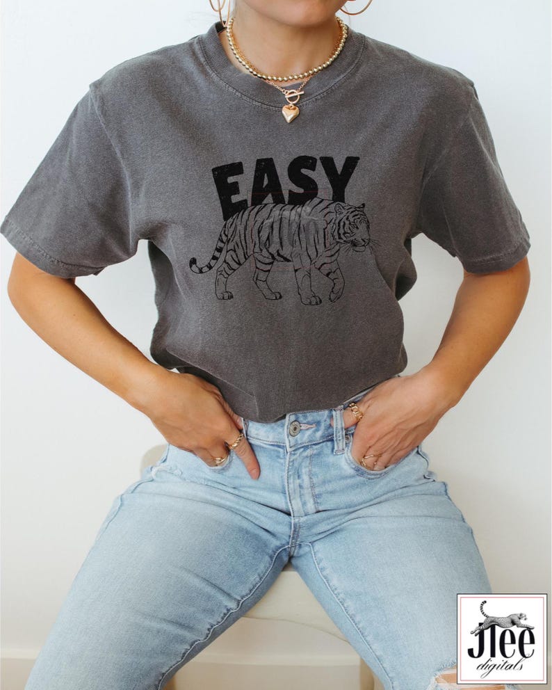 May include: A gray t-shirt with the word "EASY" printed in black letters and a black line drawing of a tiger. The tiger is walking to the right.