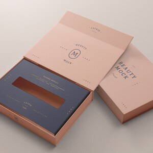 Puede incluir: Una caja de color rosa claro con una ventana recortada en la parte superior. La caja est&aacute; abierta y el interior es de color azul oscuro. La caja tiene el texto "BEAUTY MOCK" impreso en el lateral. La caja est&aacute; sobre una superficie gris claro.