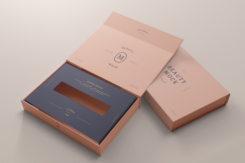 Puede incluir: Una caja de color rosa claro con una ventana recortada en la parte superior. La caja est&aacute; abierta y el interior es de color azul oscuro. La caja tiene el texto "BEAUTY MOCK" impreso en el lateral. La caja est&aacute; sobre una superficie gris claro.