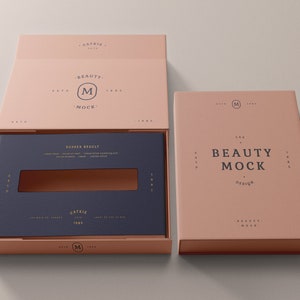 May include: A pink box with a blue insert and a gold logo that says "The Beauty Mock Design". The box is open and the insert is visible. The insert has a small window cut out of it.