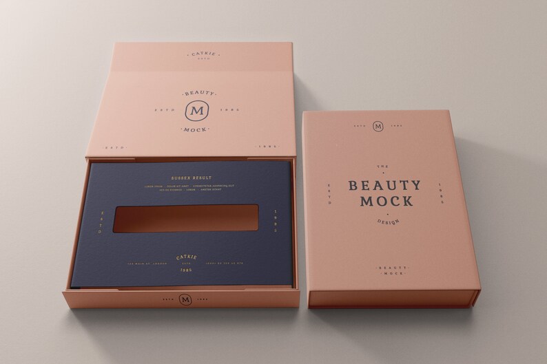 May include: A pink box with a blue insert and a gold logo that says "The Beauty Mock Design". The box is open and the insert is visible. The insert has a small window cut out of it.