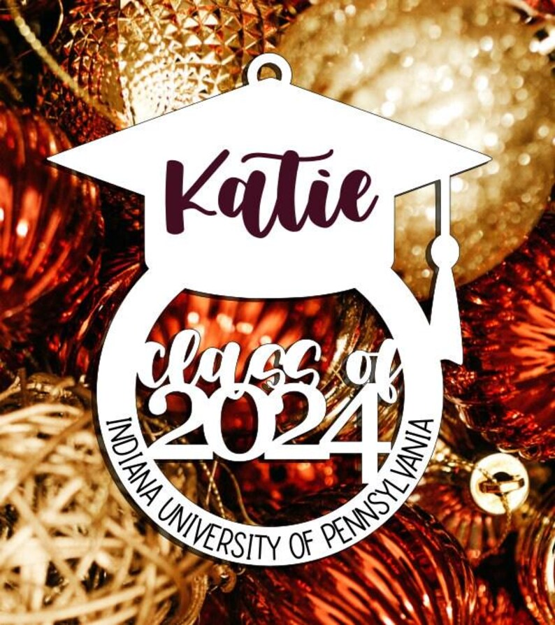 Puede incluir: Adorno de gorro de graduaci&oacute;n blanco con el nombre "Katie" y el texto "Class of 2024 Indiana University of Pennsylvania".