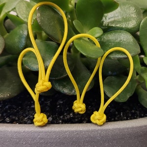 May include: Three yellow cord loops with knots at the ends. The loops are arranged in a semi-circle and are resting on top of a pot of green plants.