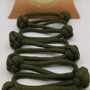 Puede incluir: Seis cierres de palanca de paracord verde con un extremo anudado. Las palancas están dispuestas en una pila, con los extremos anudados mirando hacia el espectador.