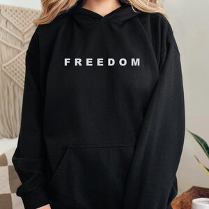 May include: Black hoodie with the word "FREEDOM" printed in white across the chest. The hoodie has a front pocket and a hood with a drawstring. The garment is made of a soft material.