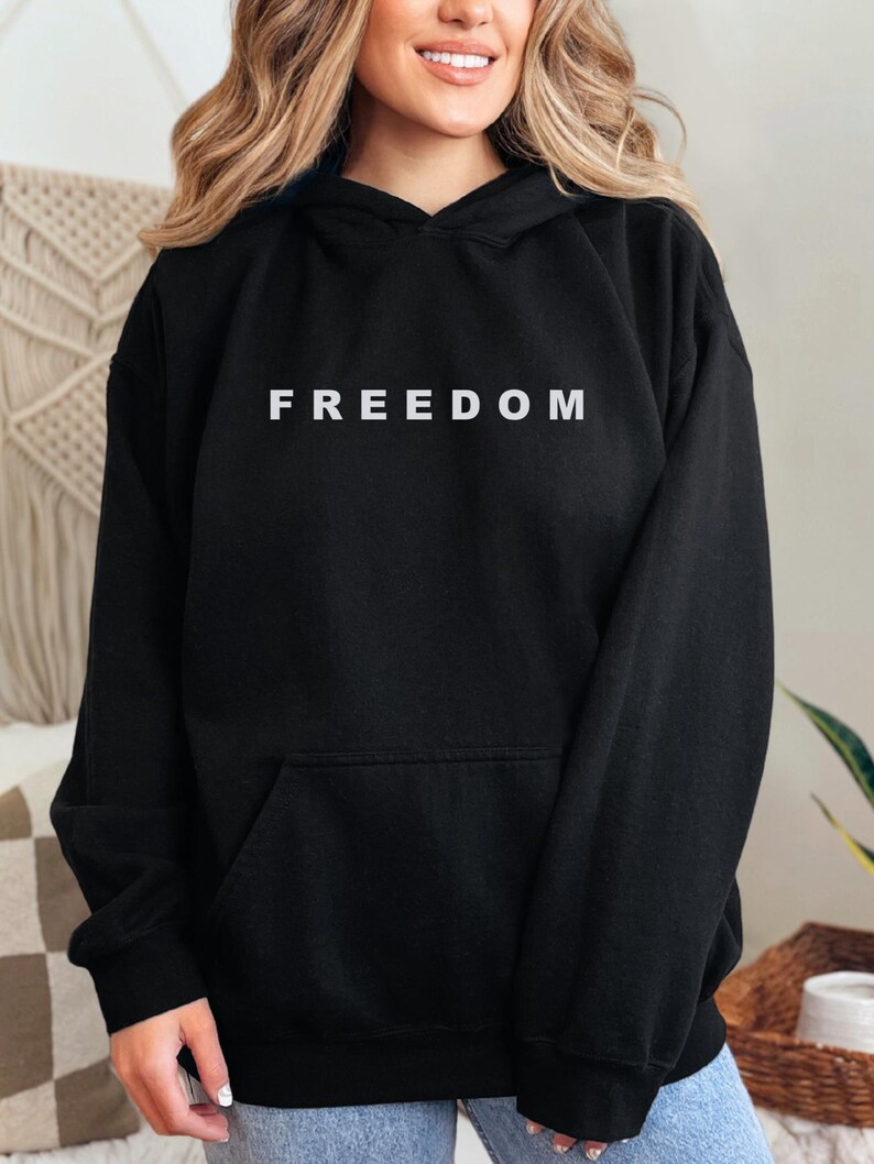 May include: Black hoodie with the word "FREEDOM" printed in white across the chest. The hoodie has a front pocket and a hood with a drawstring. The garment is made of a soft material.