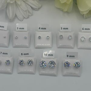 May include: A collection of sterling silver stud earrings in various sizes, from 2 mm to 10 mm, displayed on white cards. Each card is labeled with the size in millimeters. The earrings are round and have a sparkling appearance.